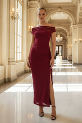 Woman in a burgundy off-shoulder dress standing in an elegant hallway with high ceilings and large windows.
