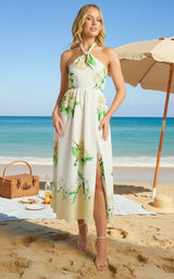 Woman in a floral dress standing on a beach with blue sky and ocean.