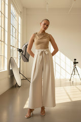 Woman wearing a beige sleeveless top and wide-leg pants on a white background