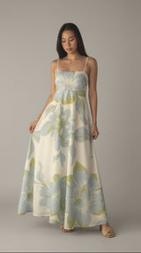 Woman wearing a floral dress taking a mirror selfie against a white curtain.